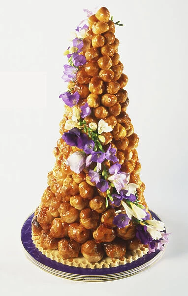 Croquembouche, French wedding cake of profiteroles filled with pastry cream, coated with caramel and decorated with small lilac flowers