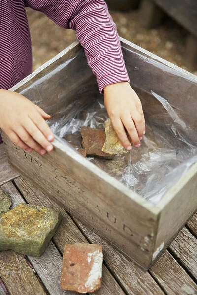 Girl placing rocks in wooden box lined with plastic