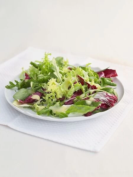 Green and red leaf salad on white plate with napkin on table