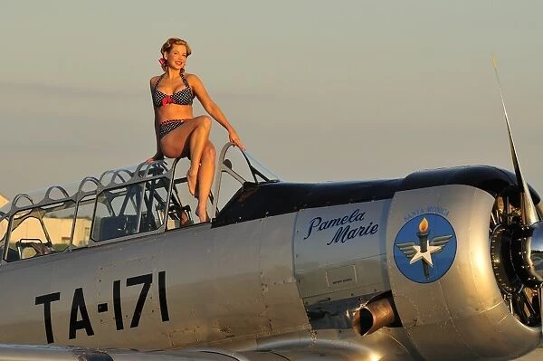 1940s style pin-up girl sitting on the cockpit of a World War II T-6 Texan