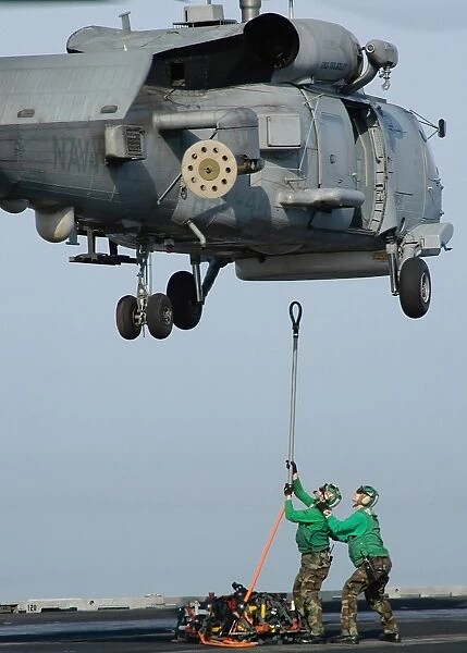 Airmen assist each other as they hook a sling to an SH-60B Seahawk
