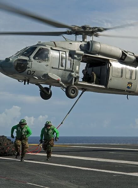Airmen run to cover after attaching cargo legs to an MH-60S Sea Hawk