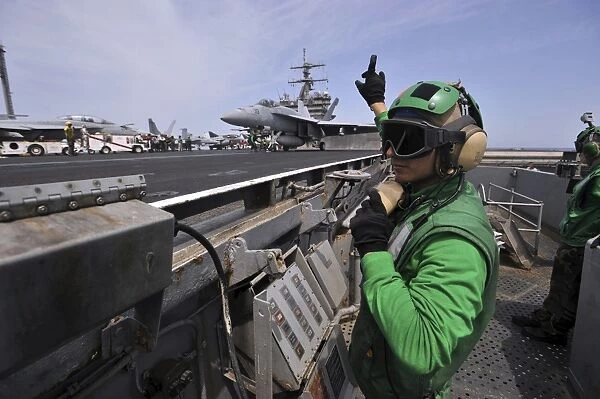 Aviation Boatswainas Mate signals to a shooter as an F  /  A-18E Super Hornet prepares
