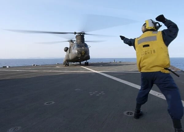 Boatswains Mate signals to an Army CH-47 Chinook helicopter