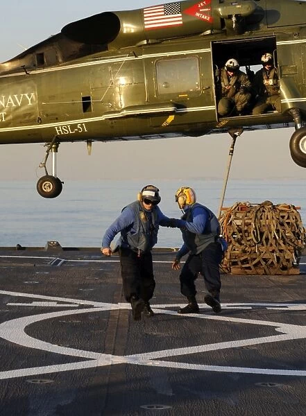 Boatswains Mates move away after connecting a hoisting sling onto an SH-60F Sea Hawk