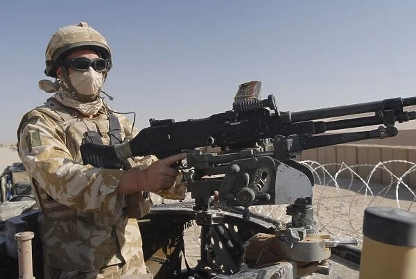 A British Army soldier mans a machine gun mounted on top of a land rover