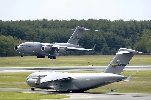 A C-17 Globemaster III performs touch and go landings while another prepares for take-off