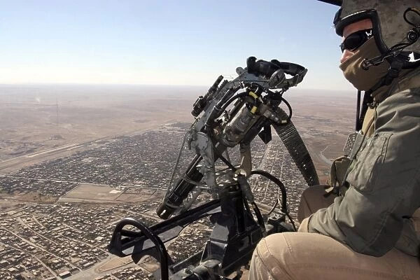 A crew chief looks for suspicious activity while manning a machine gun aboard a helicopter