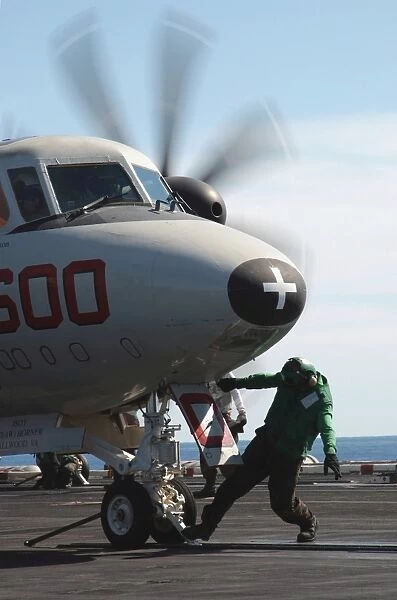 A flight deck crew member performs final checks on an E-2C Hawkeye
