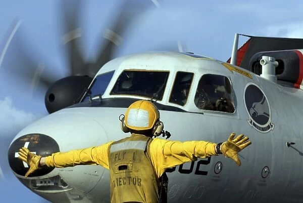 A flight deck director signals the pilot of an E-2C Hawkeye to spread his wings