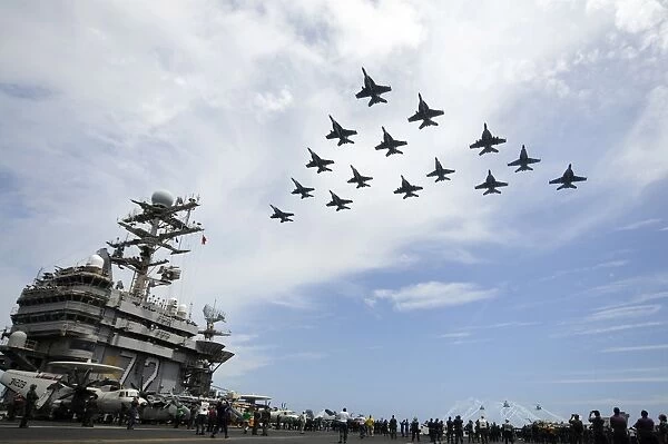 Helicopters fire flares as jets fly in formation above the flight deck of USS Abraham
