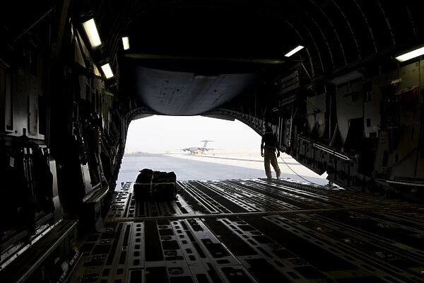 A loadmaster guides the pilot of a C-17 Globemaster III as it reverses on the runway