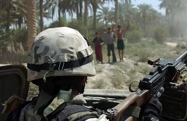 Local Iraqi children wave to a Polish Army Soldier manning a 7. 62 mm PK machine gun