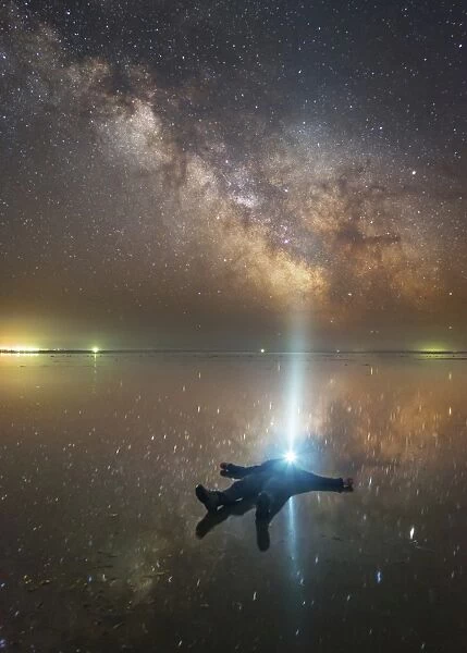 Man lying on Lake Elton in Russia under the Milky Way while shining a flashlight up