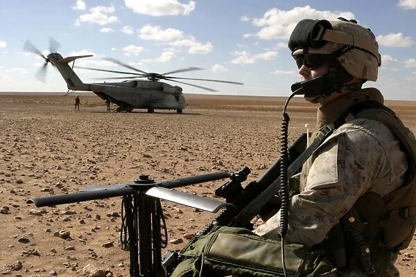 A Marine assembles a radio antenna as a CH-53E Super Stallion helicopter lands nearby