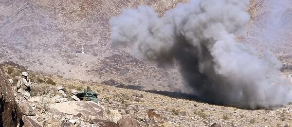Marines perched atop Machine Gun Hill watch down range as explosives detonate