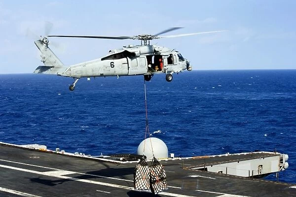An MH-60R Seahawk helicopter places cargo onto the flight deck of USS Nimitz