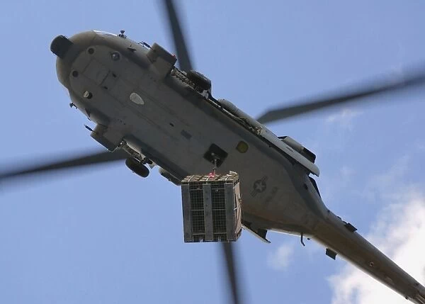 An MH-60S Seahawk helicopter airlifts a pallet of ammunition