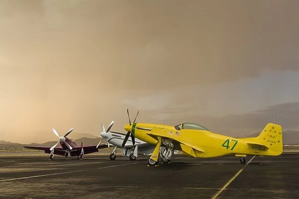 Three P-51 Mustangs parked on the ramp ahead of a storm