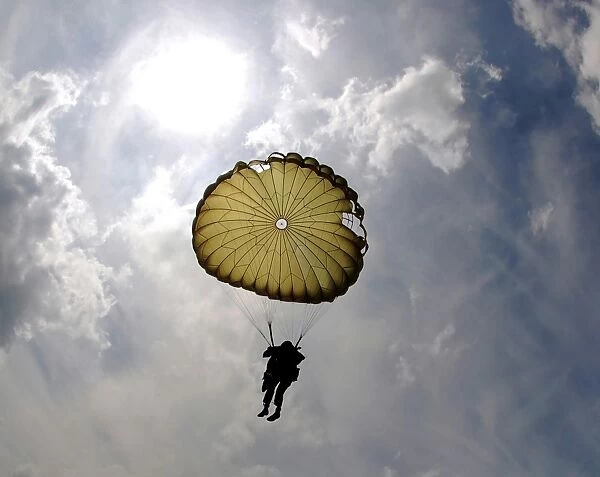 A paratrooper descends through the sky during the day