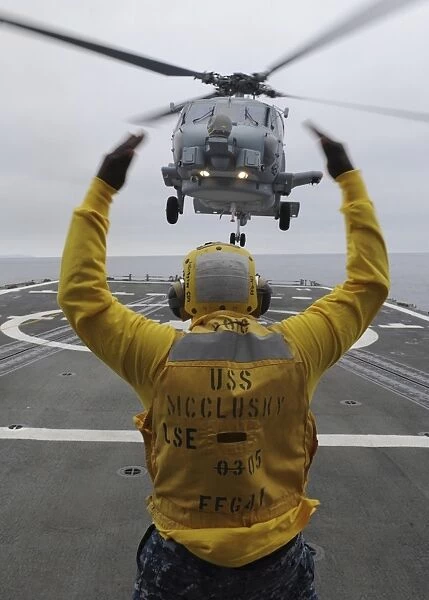 Petty Officer guides an SH-60R Sea Hawk helicopter onto the flight deck of USS McClusky