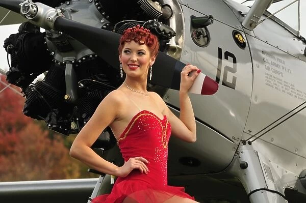 Redhead pin-up girl in 1940s style dancer attire holding on to a vintage aircraft