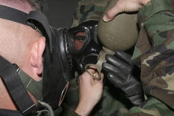 A solder assists a Marine in helping him fit his gas masks drinking tube into his