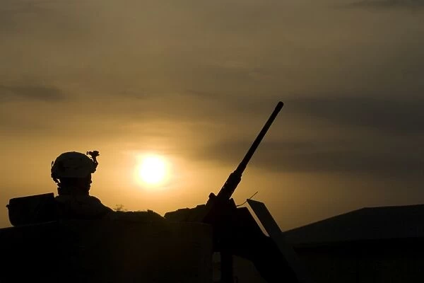 A US Soldier mans his. 50 caliber while waiting to move out on a mission at sunset