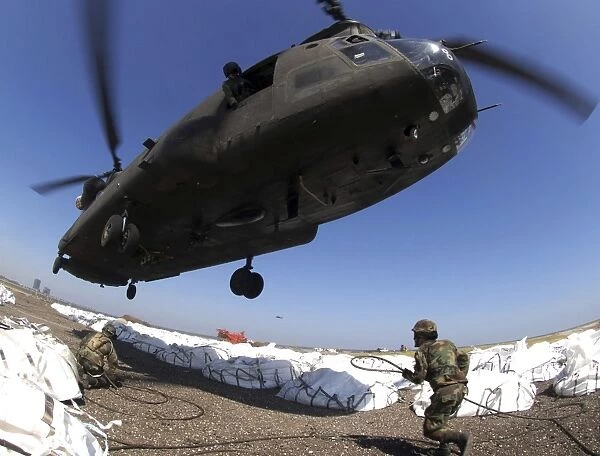 Specialists attach cargo hooks supporting large bags of sand to a CH-47 Chinook helicopter