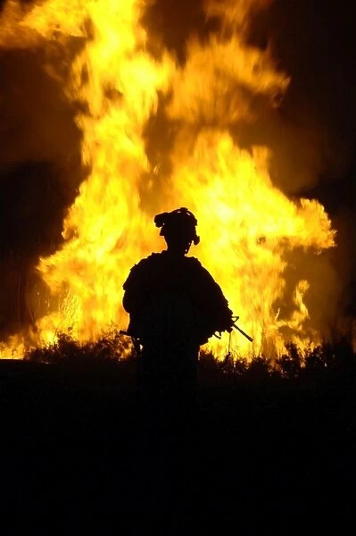 U. S. Army Sergeant monitors the flames of a fire around a canal