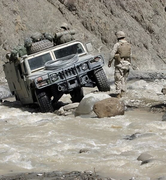 A U. S. Marine guiding the driver of a Humvee through a river in Khowst Province of
