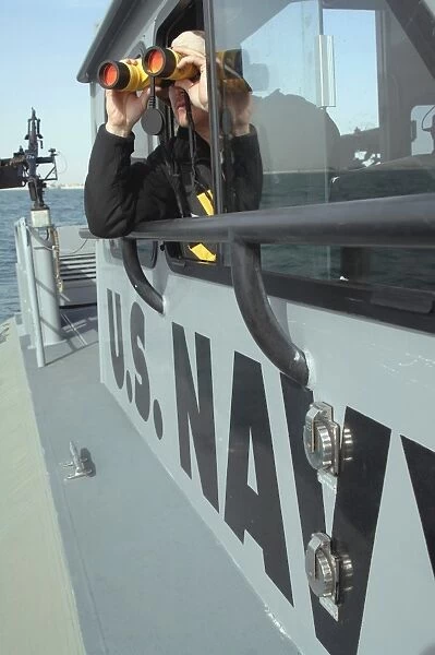U. S. Navy Boatswains Mate looks through binoculars as he patrols the coastal waters