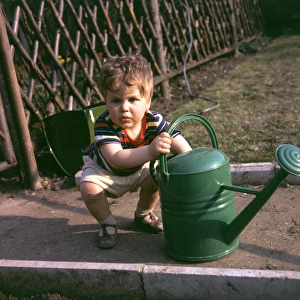 Little boy with green watering can in a garden