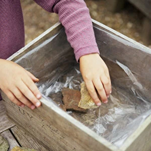 Girl placing rocks in wooden box lined with plastic