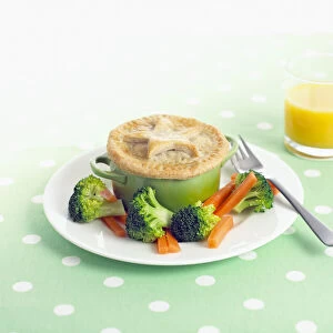 Meat and vegetable pastry pie with fork on white plate and glass of fresh orange juice on polka dot tablecloth, close-up