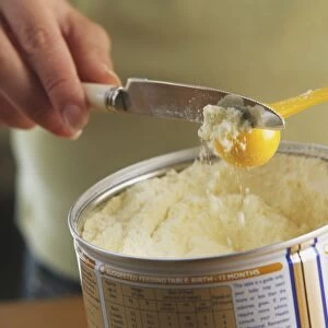 Using knife to level off yellow plastic scoop full of infant formula