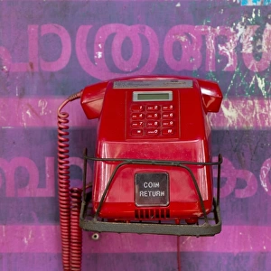 Old red telephone against a wall with pink Malayalam script, Kerala, India