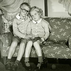 Young boy and girl dressed as adults sitting on sofa, portrait
