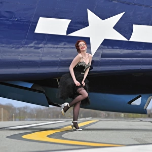 1940s style pin-up girl in cocktail dress posing in front of a TBM Avenger