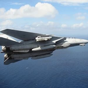 An F-14D Tomcat banks with its tailhook lowered in preparation for landing