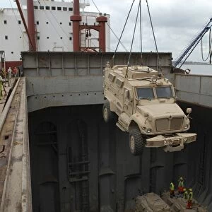 A harbor crane lifts a mine-resistant, ambush-protected vehicle from the hull of
