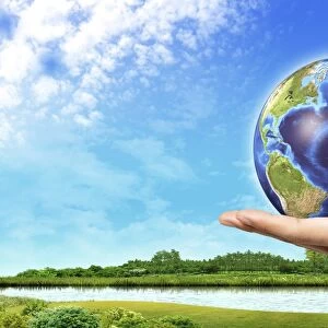 Human hand holding Earth globe with a green landscape background