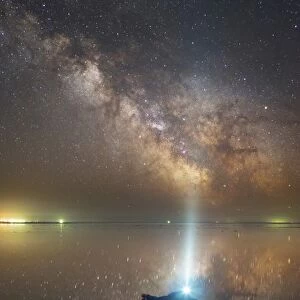 Man lying on Lake Elton in Russia under the Milky Way while shining a flashlight up