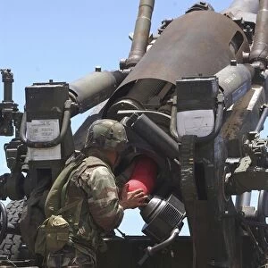 Soldier loads a charge round behind the ammunition round of the Howitzer 150 gun
