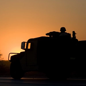 A U. S. Army Humvee with soldiers in the back at sunset
