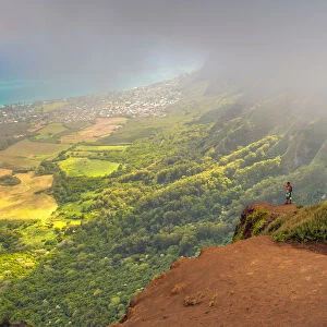 A Man Standing On The Edge Of A Cliff On The Kuliouou Ridge Trial Enjoys The View Of Oahus Windward Side And The Town Of Waimanalo As The Clouds Roll In On A Summers Day; Waimanalo, Oahu, Hawaii, United States Of America