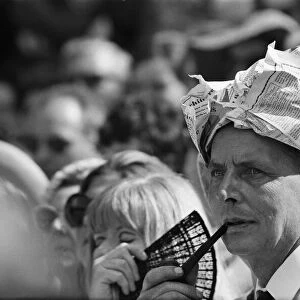 A man smoking a pipe, wearing his newspaper as a hat watches Wimbledon Tennis